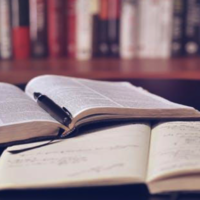 2 books open on a desk with a pen sitting on one of them