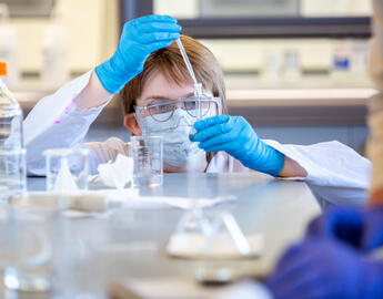 A young student in a lab holds a dropper over a beaker.