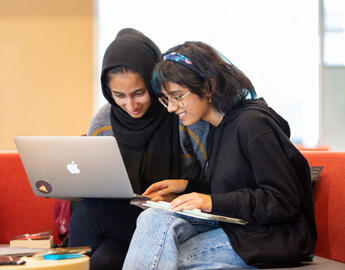 Two UCalgary students work on a laptop in the library