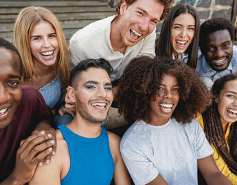 A group of diverse young people sit close together and smile.