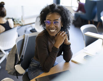A young Black woman sits at a work table and smiles.