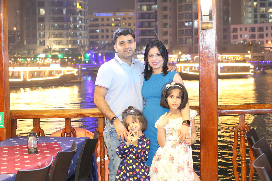 Two parents and two little girls stand smiling at the camera on a deck overlooking a body of water