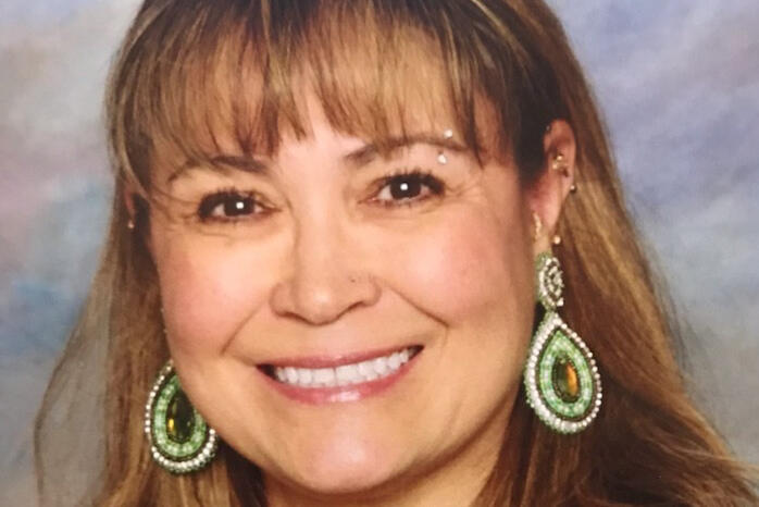 A woman with brown hair wearing beaded earrings smiles at the camera