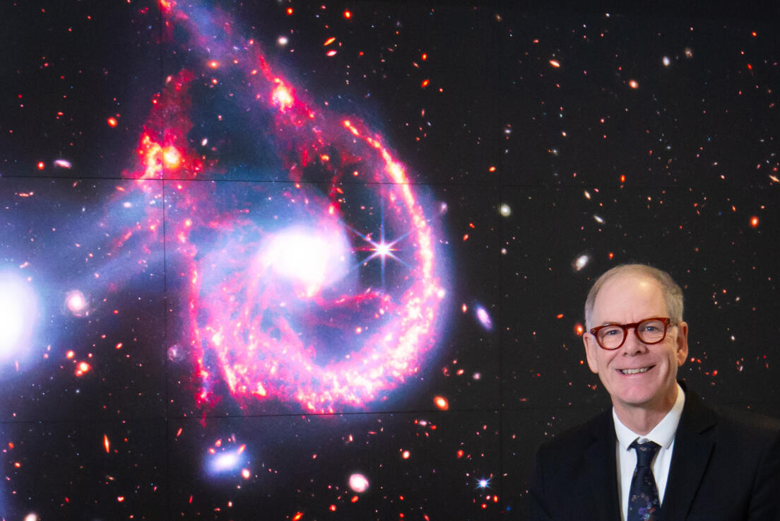 A man sits in front of a photo of outer space
