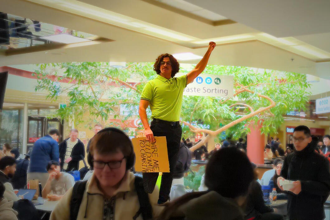 A man stands on a table in a crowded cafeteria