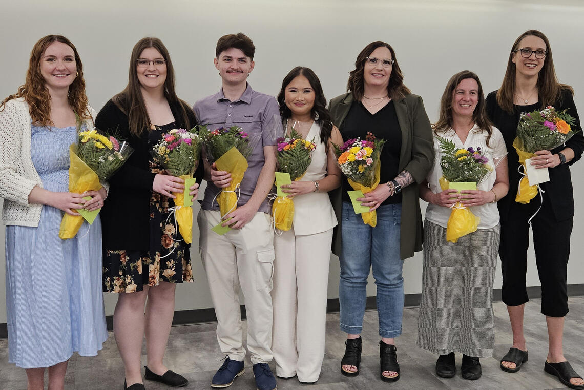 A group of people stand in a line holding bouquets of flowers